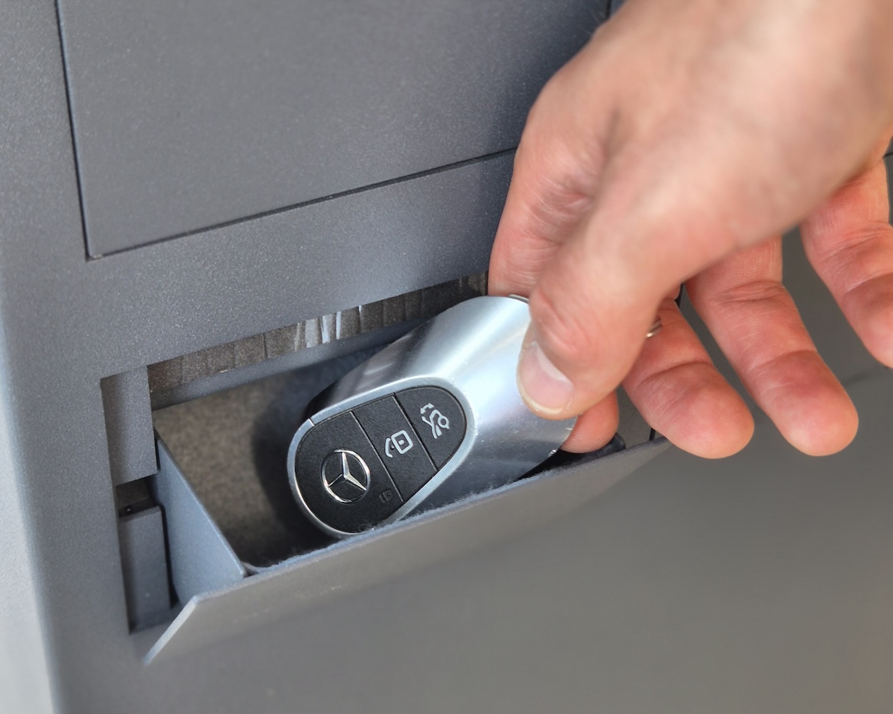 Na zdjęciu widzisz rękę mężczyzny sięgającą po kluczyk leżący w skrytce w kluczykomacie.