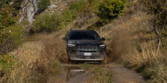 Na zdjęciu widzisz Jeepa Compass w kolorze ciemnozielonym jadącego po błotnistej drodze.